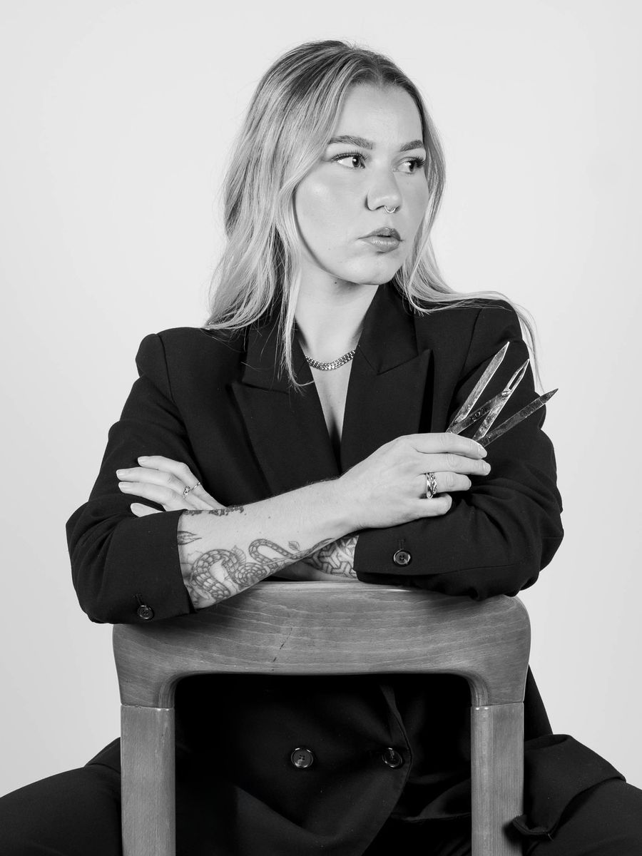 Tatjana, Gründerin von TALAJ Studio, sitzt mit Pinzetten in der Hand auf einem Stuhl (Schwarz-Weiss-Porträt)